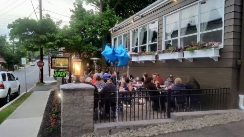 Outdoor dining scene at a restaurant with patrons enjoying their meals, colorful balloons, and an "Open" sign.