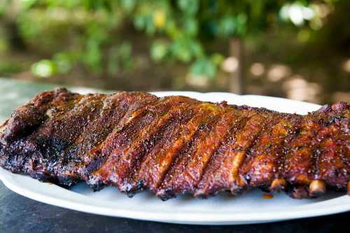 A plate of succulent, smoky barbecue ribs with a crispy, caramelized glaze, set against a blurred green background.