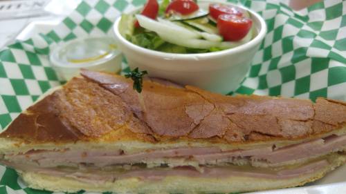 A close-up of a sandwich with layers of ham and cheese, served with a side salad in a bowl.