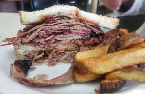 A close-up of a stacked sandwich filled with layers of meat, served with golden-brown fries on the side.