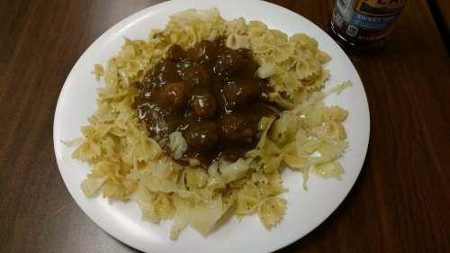 A plate of bowtie pasta topped with meatballs and brown gravy, served with a side of cabbage.