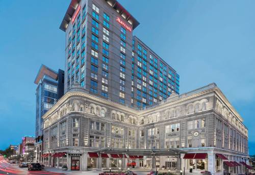 A modern Marriott hotel building with a historic facade, illuminated at dusk, surrounded by city streets and flowers.