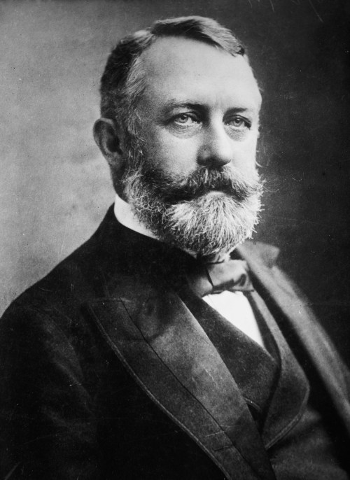 A black and white portrait of a man with a beard, wearing a suit and bow tie, looking thoughtfully at the camera.