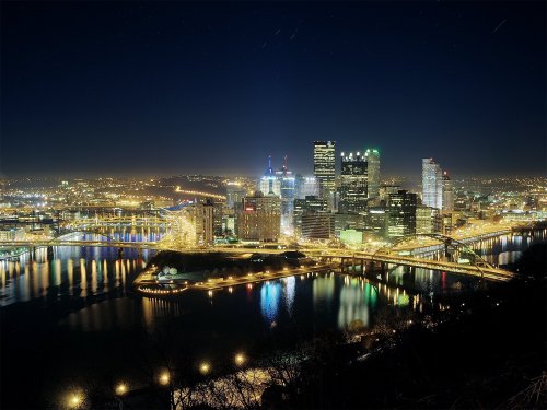 A nighttime view of Pittsburgh's skyline, illuminated buildings reflecting on the river below.