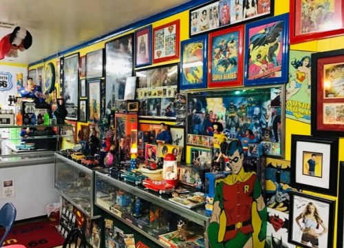 A colorful room filled with superhero memorabilia, posters, and collectibles displayed on walls and shelves.
