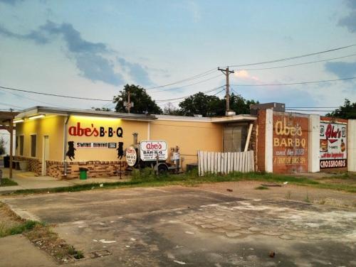 Exterior of Abe's BBQ restaurant with signage, a white fence, and a cloudy sky in the background.