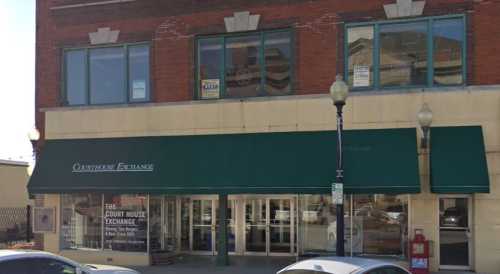 Exterior of a brick building with large windows and a green awning, featuring signage for "The Court House Exchange."