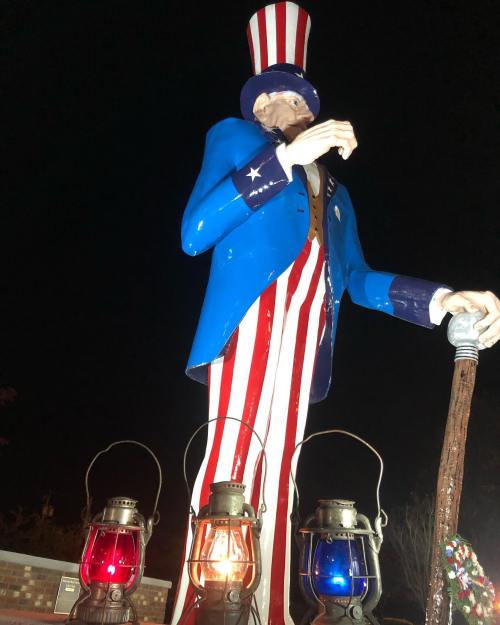 A large Uncle Sam statue in a blue coat and red-striped pants, illuminated by red and blue lanterns at night.
