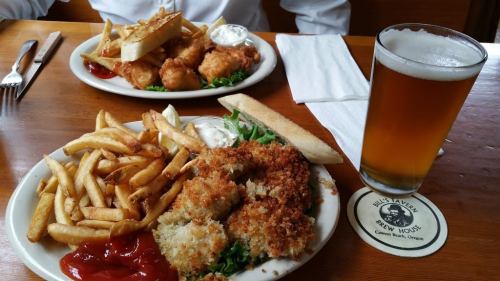 A plate of fried seafood with fries and dipping sauces, alongside a glass of beer and another plate of food in the background.