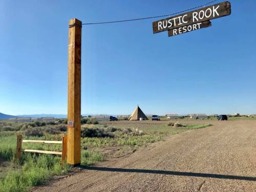 Sign for Rustic Rook Resort at the entrance, with a teepee and vehicles in the background under a clear blue sky.