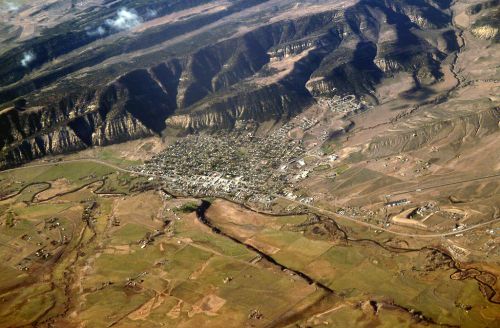 Aerial view of a small town surrounded by mountains and fields, with winding rivers and patches of greenery.