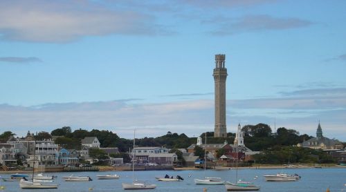 A coastal scene featuring boats in the water and a tall tower overlooking a charming town with houses.
