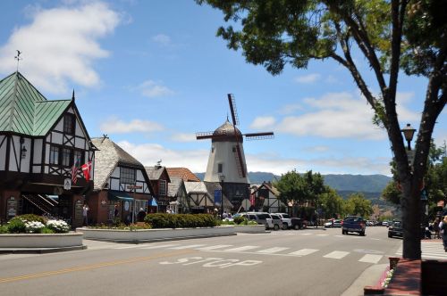 A charming street scene featuring quaint buildings and a windmill under a blue sky with fluffy clouds.