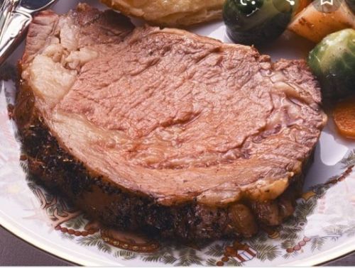 A slice of juicy roast beef on a decorative plate, accompanied by vegetables.