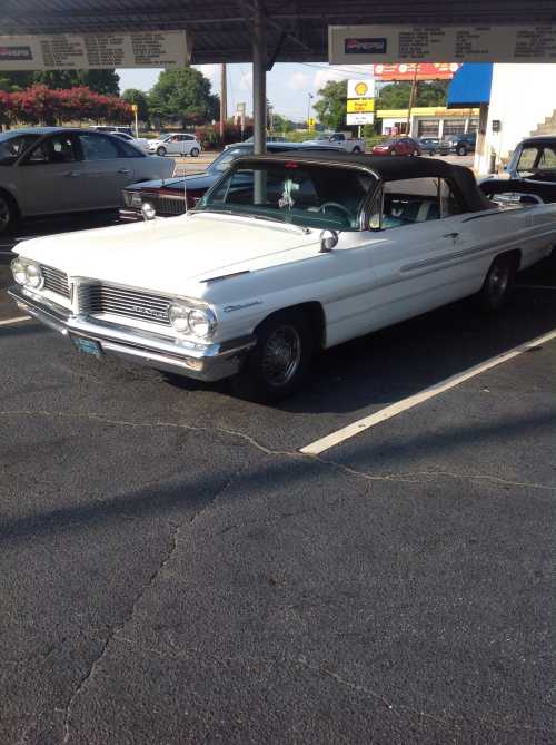 A classic white convertible car parked under a canopy, with a black soft top and vintage styling.