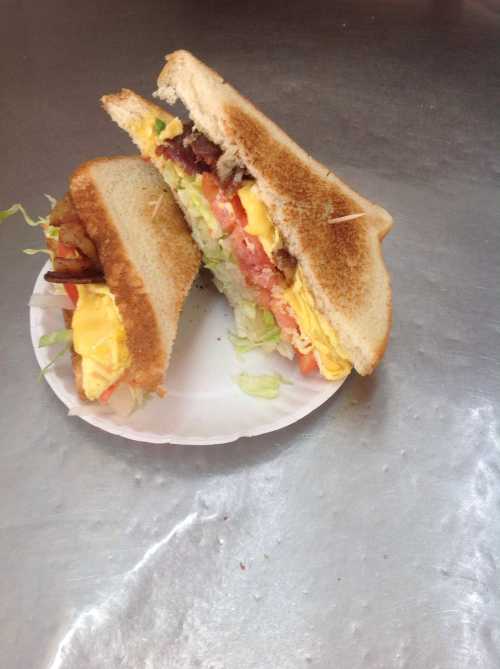 A sandwich with layers of lettuce, tomato, cheese, and bacon, served on a white plate against a metallic background.