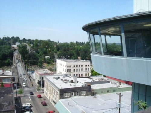 Aerial view of a cityscape featuring a modern building with a glass observation area and surrounding urban landscape.