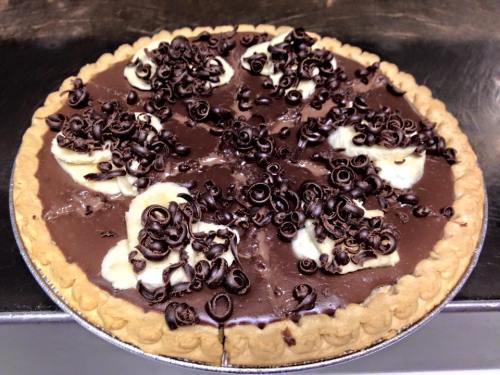 A chocolate pie topped with banana slices and chocolate curls on a golden crust.