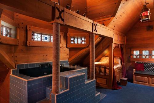 Cozy wooden interior of a unique bedroom with a raised bed, decorative windows, and a small sunken tub.