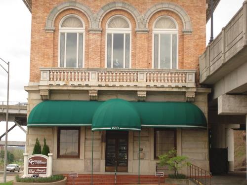 Historic brick building with large windows, a green awning, and decorative balcony, located under a bridge.