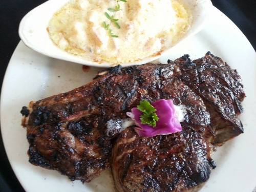 A plate featuring grilled steak with a purple flower garnish and a side of creamy baked dish.
