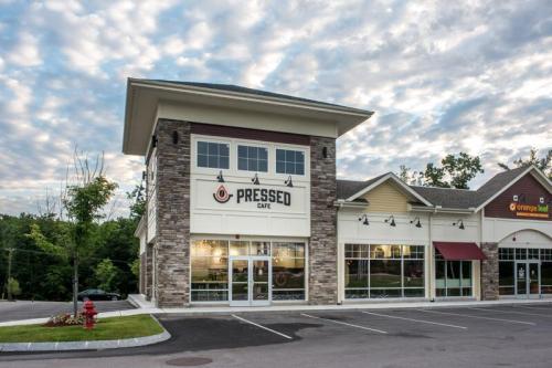 Exterior of Pressed Cafe, a modern building with stone accents, surrounded by a parking lot and cloudy sky.