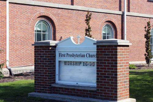 Sign for First Presbyterian Church displaying "WORSHIP 10:30" in front of a brick church building.