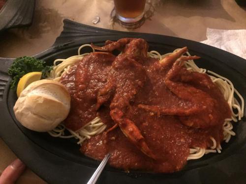 A plate of spaghetti topped with crab in a rich red sauce, served with a lemon wedge and a bread roll.