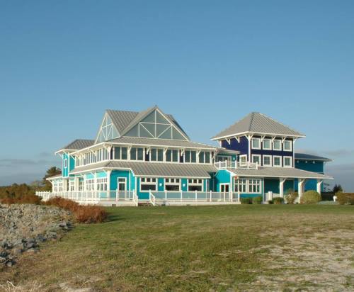 A large, modern blue house with multiple gables and a spacious lawn, set against a clear sky.