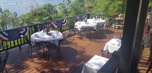 Outdoor dining area with tables set for guests, decorated with red, white, and blue bunting, overlooking a scenic view.