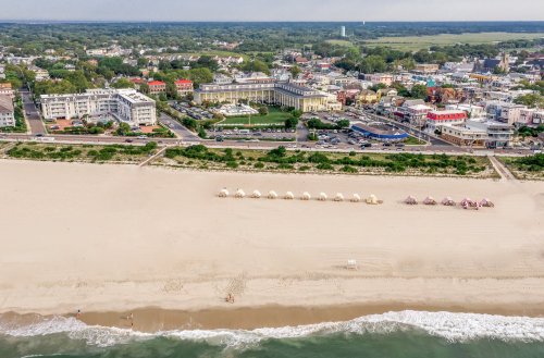 Aerial view of a beach with umbrellas, sandy shore, and a colorful coastal town in the background.