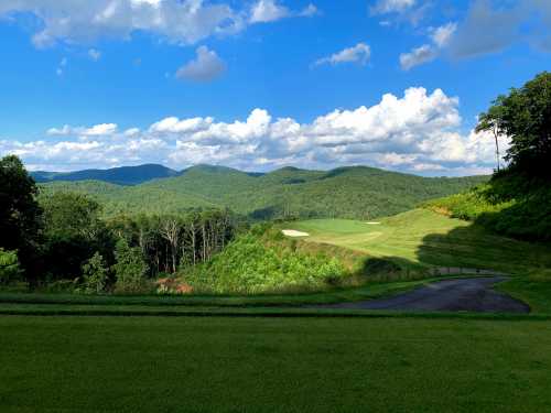 A scenic view of rolling green hills and a golf course under a blue sky with fluffy clouds.