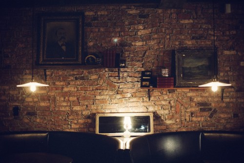 Cozy interior with a brick wall, vintage paintings, and warm lighting from hanging lamps and a table lamp.