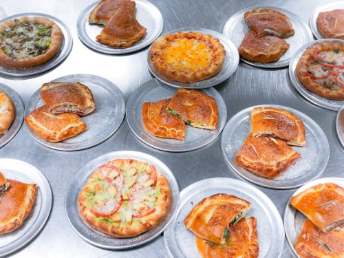 A variety of savory pastries and pizzas on metal plates, arranged on a silver surface.
