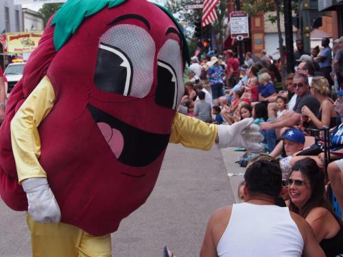 A large, smiling chili pepper mascot interacts with a crowd at a festive outdoor event.