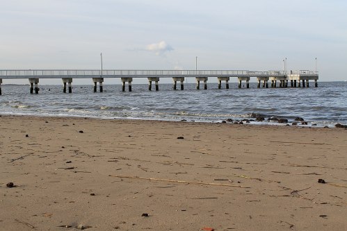 A sandy beach with a wooden pier extending over calm water under a cloudy sky.
