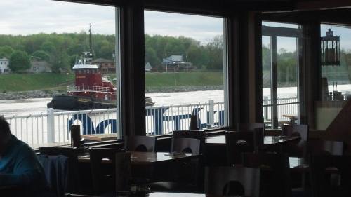 A tugboat navigates a river, viewed through a restaurant window with empty tables in the foreground.