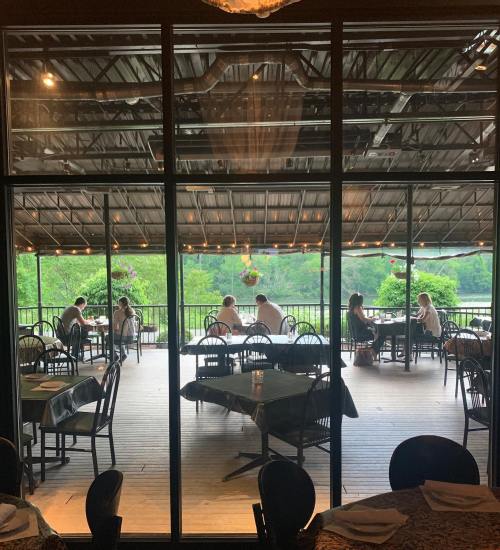 A view through glass doors of a restaurant patio with diners enjoying a meal surrounded by greenery.