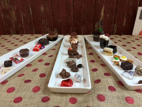 Three white trays filled with an assortment of chocolates and desserts, arranged neatly on a polka dot tablecloth.