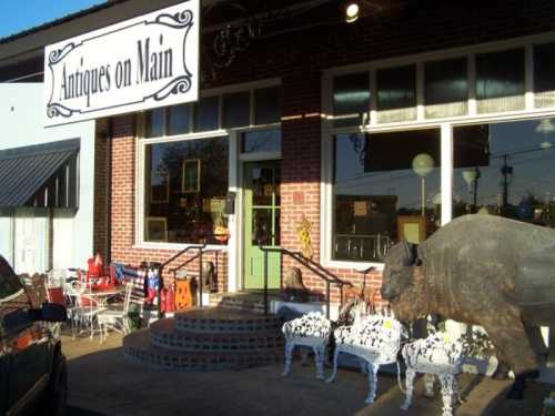 A storefront labeled "Antiques on Main" featuring a large buffalo statue and decorative chairs outside.