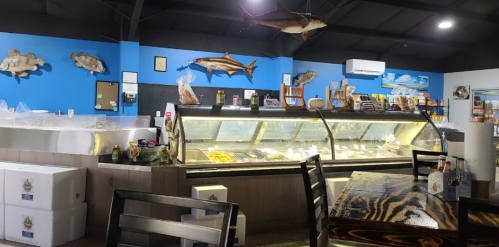 Interior of a seafood market with a display case, wooden tables, and fish decorations on the walls.