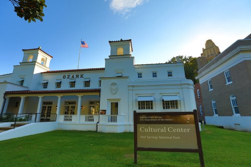 Historic building with a sign for the Cultural Center at Hot Springs National Park, surrounded by green grass and trees.