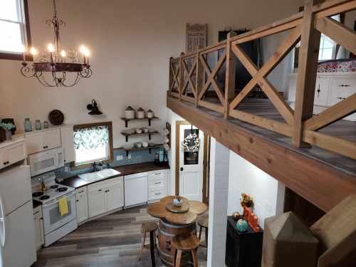 A cozy kitchen with wooden accents, a round table, and a loft area visible above, featuring a chandelier and decor.