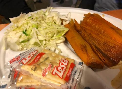 A plate with tamales, shredded cabbage, and two packets of crackers.