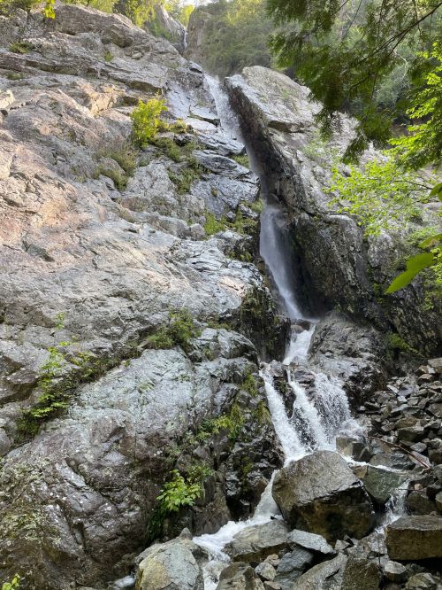 A cascading waterfall flows down rocky terrain, surrounded by lush greenery and steep cliffs.