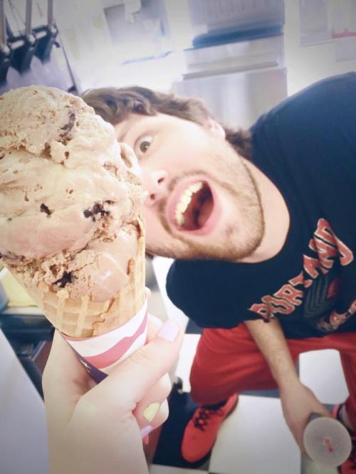 A person excitedly looks at a large ice cream cone held in front of them, with a playful expression.