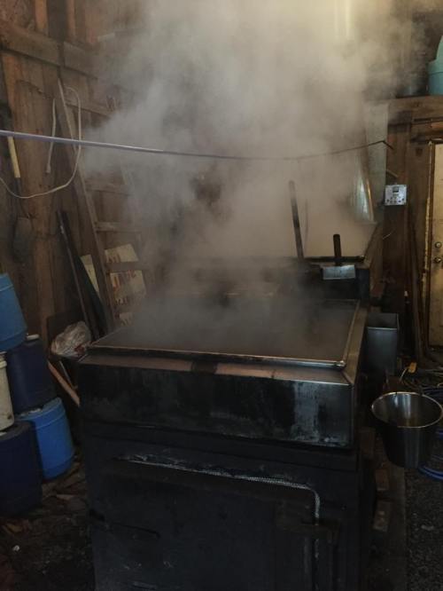 A large metal cooking pot emits thick steam in a rustic kitchen setting.