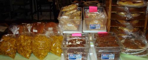A display of various packaged snacks and baked goods in clear containers and bags at a market stall.