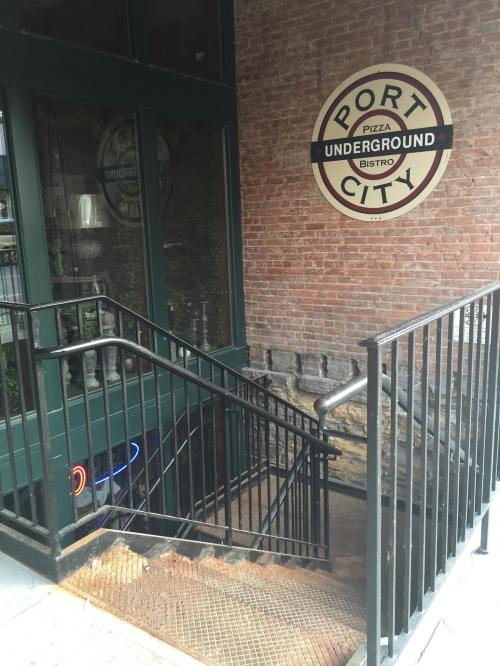 Stairs leading down to a restaurant entrance with a "Port City Pizza Underground Bistro" sign on a brick wall.