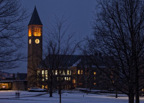 A clock tower illuminated at dusk, surrounded by snow-covered trees and a winter landscape.